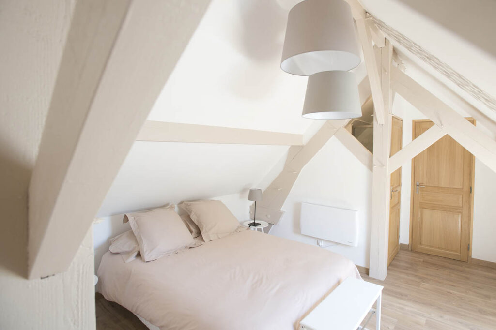 Chambre sous les toits avec poutres et tons taupe, un nid douillet pour des nuits paisibles.